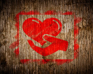 Charity. Red Icon of Heart in the Hand Painted by Stencil on Wood. Grunge Background.