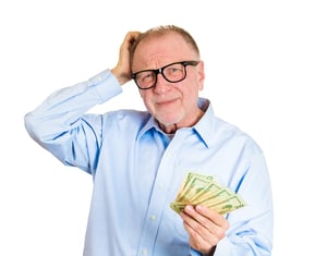 Closeup portrait, nerd senior mature man, black glasses, holding money in one hand, scratching head, not sure how to spend extra cash dollar bills, isolated white background. Human emotion, expression